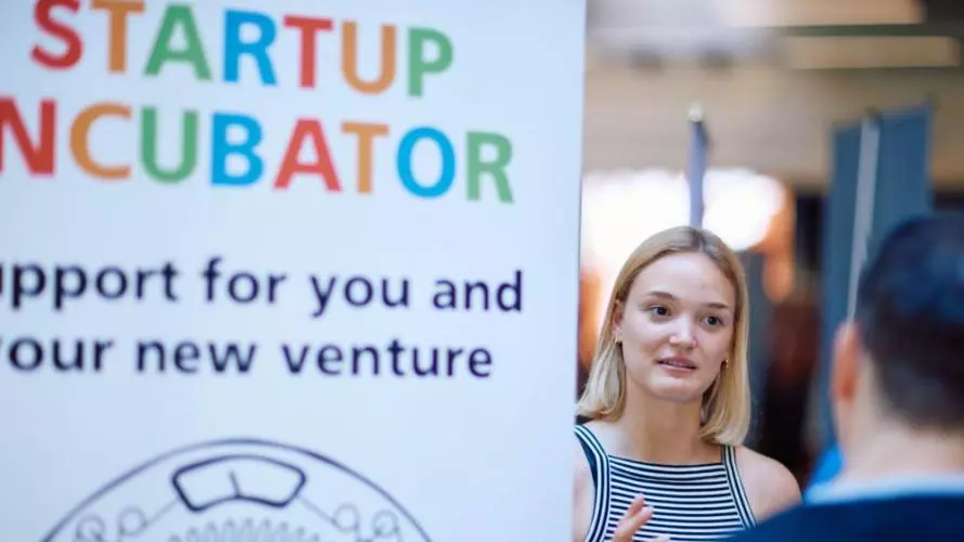 A women talking to somebody stood next to a Startup Incubator pull up banner