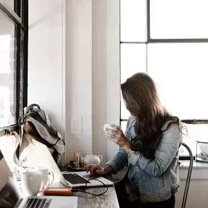 Woman holding a coffee cup working at a laptop at a desk