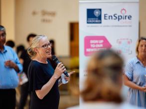 Kylie Vincent talking at the Demo Night 2023 event with an EnSpire banner and crowd members in the background