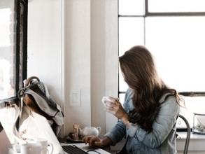Woman holding a coffee cup working at a laptop at a desk