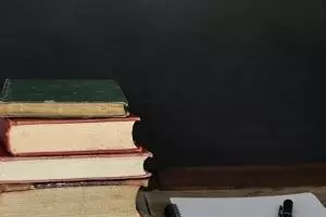 A pile of books sat next to a pad of paper and a pen