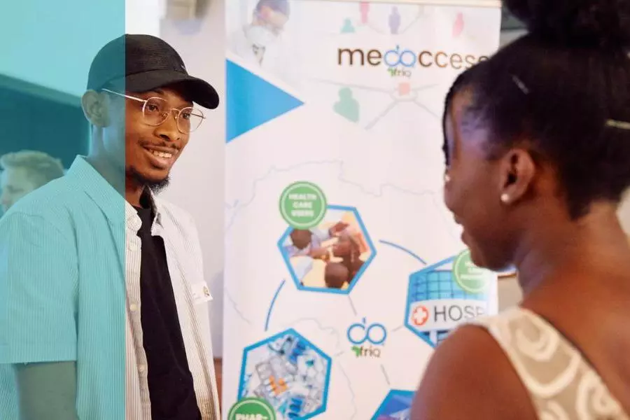 A young entrepreneur stood next to his business stand talking to an event attendee