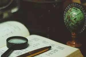 An open book sat next to a mini globe with a magnifying glass and pen