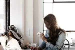 Woman holding a coffee cup working at a laptop at a desk
