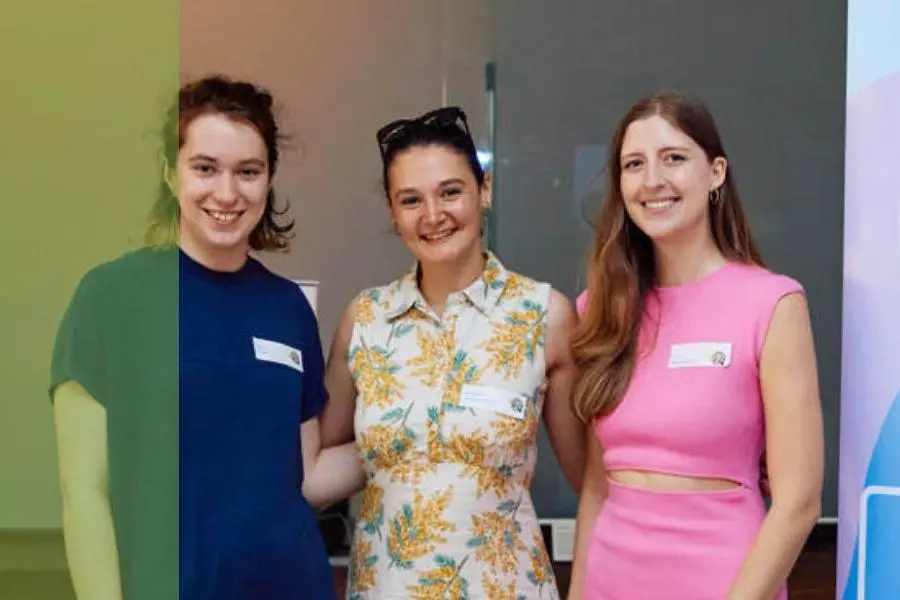 Three women entrepreneurs smiling next to their business stand at an event